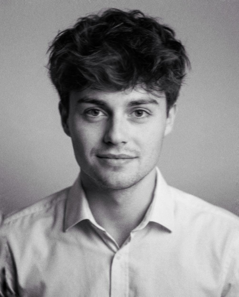 Portrait of a man with brown hair and glasses on a flat gray background.